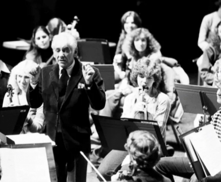 This black-and-white photo captures a moment of Leonard Bernstein conducting an orchestra rehearsal. 