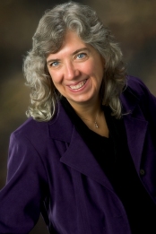 Photo of a white woman with long wavy grey hair wearing a dark purple blouse.